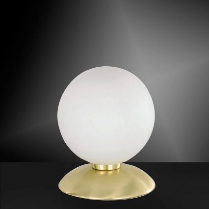 Stolová lampa s bielym skleneným guľovitým tienidlom a zlatým podstavcom stojí na tmavej ploche.