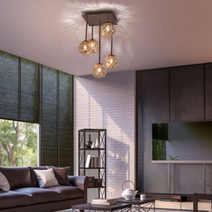 Lustr s piatimi guľovými tienidlami visí zo stropu v obývacej izbe. Tienidlá sú kovové, sieťované a zlaté. Izba obsahuje pohovku, televízor a knihovničku.