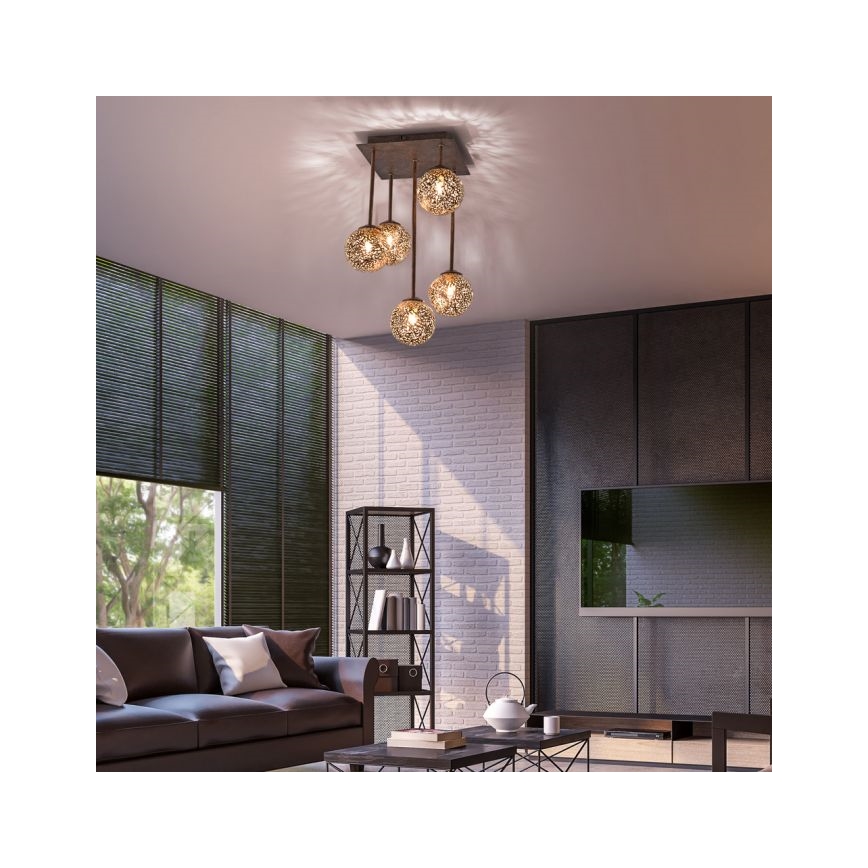 Lustr s piatimi guľovými tienidlami visí zo stropu v obývacej izbe. Tienidlá sú kovové, sieťované a zlaté. Izba obsahuje pohovku, televízor a knihovničku.