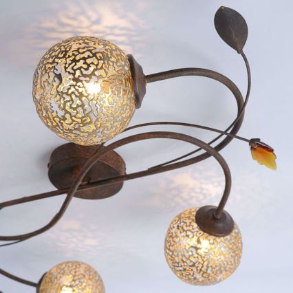 Stropné svietidlo s niekoľkými guľovitými tienidlami z perforovaného skla svieti. Kovové ramená svietidla sú tvarované ako vetvičky s listami. Svietidlo je pripevnené k stropu.