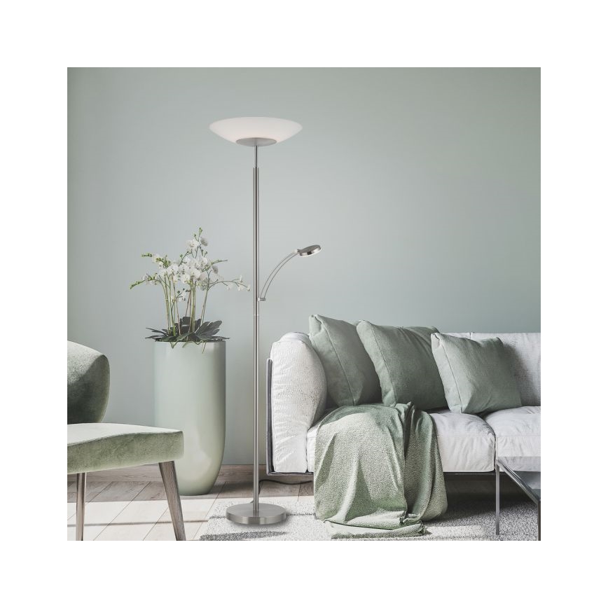 Stojacia lampa s nastaviteľnou čítacím svetlom stojí v obývacej izbe pri pohovke s vankúšmi a zelenou dekou. Vedľa je kvetináč s orchideami.