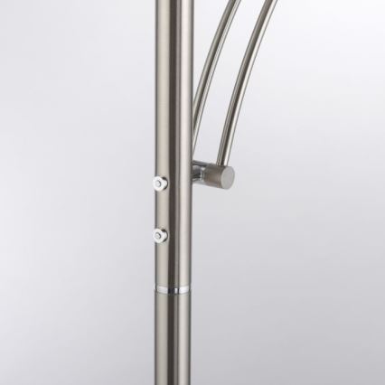 Stojacia lampa s kovovou konštrukciou a dvoma spínačmi na stĺpiku. Ohnuté ramená lampy sú pripevnené k stĺpiku. Svetlý pozadia.