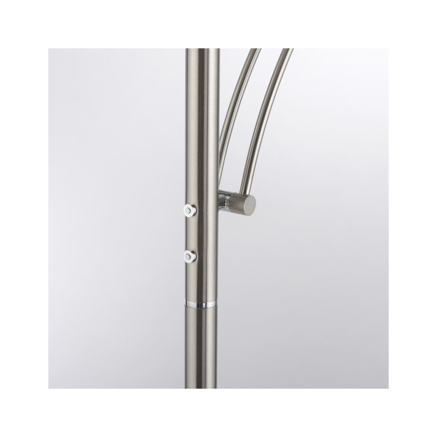 Stojacia lampa s kovovou konštrukciou a dvoma spínačmi na stĺpiku. Ohnuté ramená lampy sú pripevnené k stĺpiku. Svetlý pozadia.