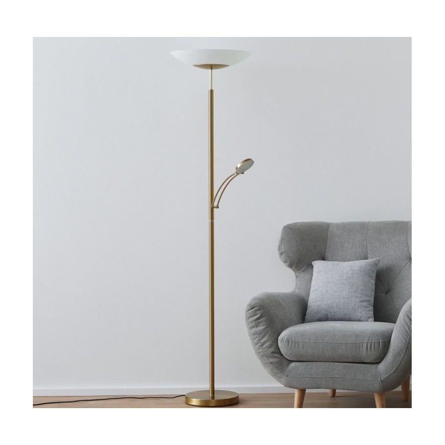 Zlatá stojacia lampa s dvoma svetlami stojí v miestnosti popri sivej kreslovej stoličke. Hlavné svetlo má široký biely tienidlo, menšie je otočné.