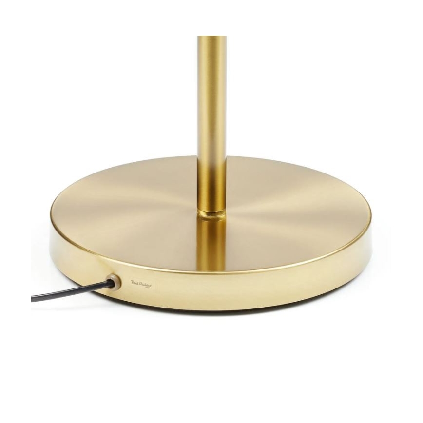 Zlatá kovová stojaca lampa s okrúhlou základňou. Na spodku základne je viditeľný nápis Paul Denleed. Stojí na svetlej ploche.