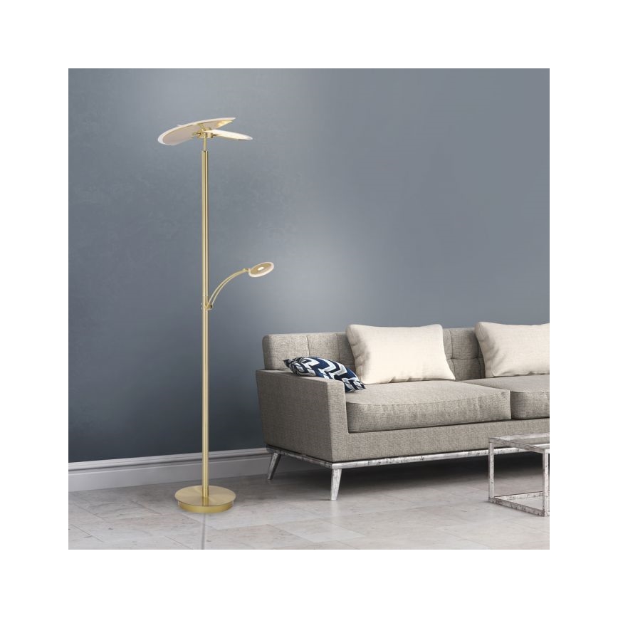 Zlatá stojaca lampa s dvoma svetlami svieti v obývacej izbe s šedou pohovkou a nízkym stolíkom.