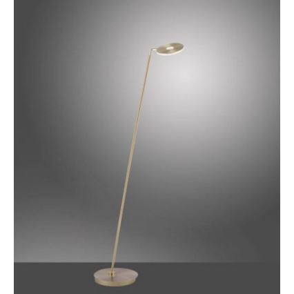 Stojacia lampa s tenkým zlatým stojanom a okrúhlou hlavou svieti. Lampa je umiestnená na neutrálnom sivom pozadí.