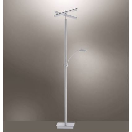 Stojacia lampa s dvoma svetelnými zdrojmi stojí na štvorcovej podstavci. Horný zdroj má krížový tvar, dolný je pohyblivý. Lampa je umiestnená na jednotnom farebnom pozadí.