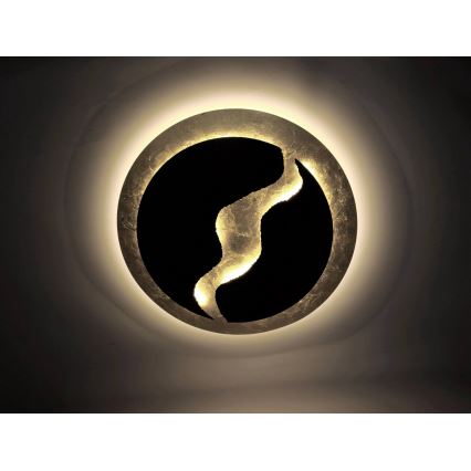 Svetlo s okrúhlym zlatým rámom a vnútorným čiernym kruhom s vyrezávaným zlatým vzorom svieti na strope.