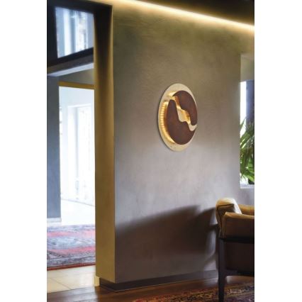 Okrúhle nástenné svietidlo s hnedým kovom a LED osvetlením je pripevnené na stene. Svietidlo osvetľuje interiér. Nachádza sa v chodbe s koženým kreslom a kobercom.