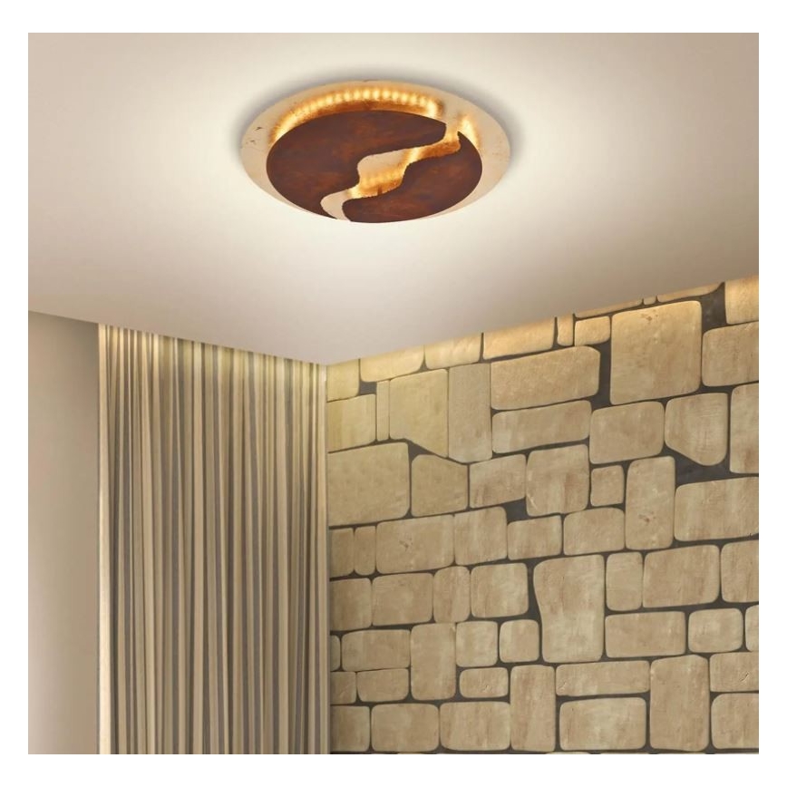 Stropné svietidlo s okrúhlym hnedo-zlatým tienidlom s abstraktným vzorom je osadené na strope. Svietidlo je osvetlené LED diódami. Stena je obložená kameňom, vedľa nej sú vertikálne pruhované závesy.
