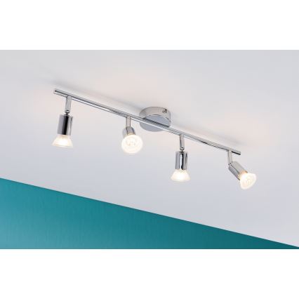 Štvorbodové stropné svietidlo s chrómovou tyčou a nastaviteľnými reflektormi je pripevnené k stropu. Svietidlo svieti v miestnosti s tyrkysovou stenou.