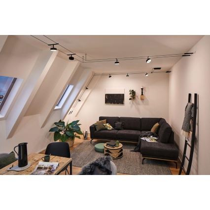 Svietidlá svietia v podkroví. Sú umiestnené na koľajniciach na strope nad tmavosivou rohovou sedačkou a jedálenským stolom. V miestnosti sú rastliny, obrazy a doplnky.