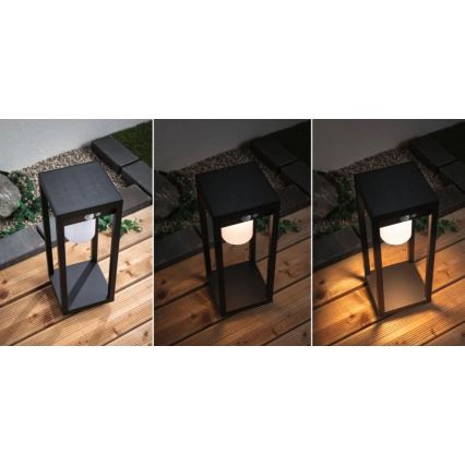 Čierna vonkajšia lampa s guľovou žiarovkou vnútri, svieti v troch fázach: vypnutá, s bielym a s teplým svetlom. Stojí na drevenom terase, v pozadí je zeleň a dlažba.