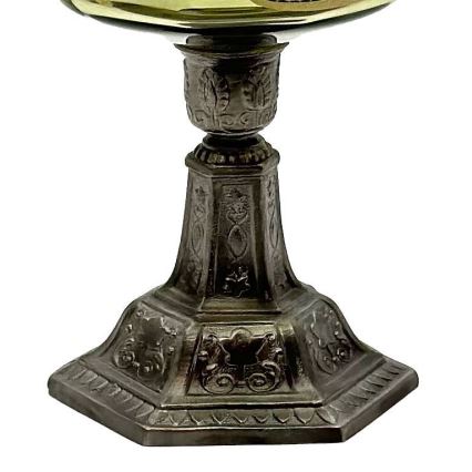 Stojan s misou z tmavého kovu s ozdobnými výrezmi stojí na bielom pozadí. Miska je svetlejšia, zlatistej farby. Stojan má viacúrovňovú podstavu s vyrezávanými ornamentmi.