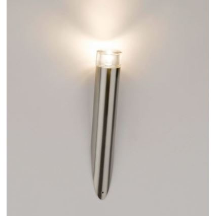 Nástenná lampa svieti. Je vyrobená z kovu, valcovitého tvaru zužujúceho sa k základni. Upevnená je na svetlej stene.