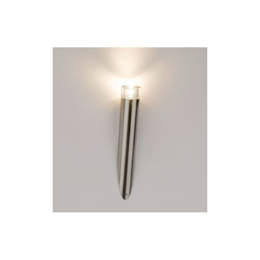 Nástenná lampa svieti. Je vyrobená z kovu, valcovitého tvaru zužujúceho sa k základni. Upevnená je na svetlej stene.