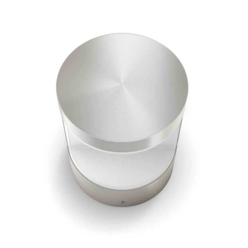 Strieborné kovové svietidlo s valcovým tvarom a kruhovým vrchnákom stojí na bielom pozadí. Svietidlo je čiastočne priesvitné.