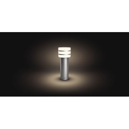 Vonkajšie svietidlo svieti na tmavom pozadí. Stĺpikové svietidlo z kovu má valcový svetelný zdroj s dvoma kovovými prstencami.