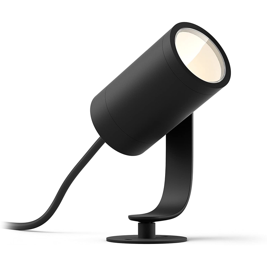 Čierna vonkajšia lampa svieti. Je pripevnená k zakrivenému čiernemu držiaku a má pripojený kábel. Lampa je umiestnená na plochej podložke.
