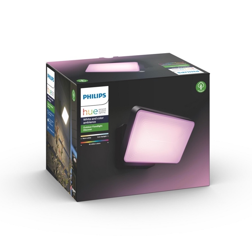 Vonkajší nástenný reflektor Philips Hue Discover svieti jemne ružovým svetlom. Je zabalený v čiernej krabici s popisom: Philips Hue, White and color ambiance, Outdoor Floodlight Discover, warm white, cool daylight, 16 miliónov farieb.