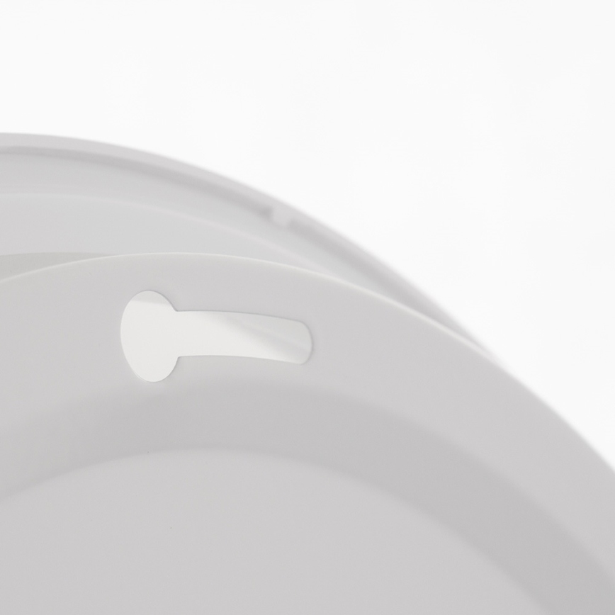 Svetlošedý plastový kruhový predmet má výrez v tvare obdĺžnika s kruhovým otvorom na jednom konci. Predmet je na bielom pozadí.