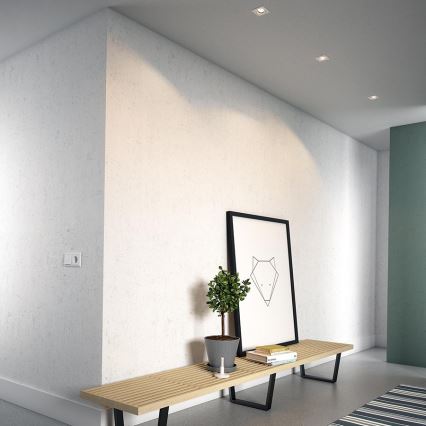 Drevená lavica s kvetináčom a obrázkom líšky stojí pri svetlej stene v chodbe. Na lavici sú knihy. Strop je osvetlený bodovými svetlami.