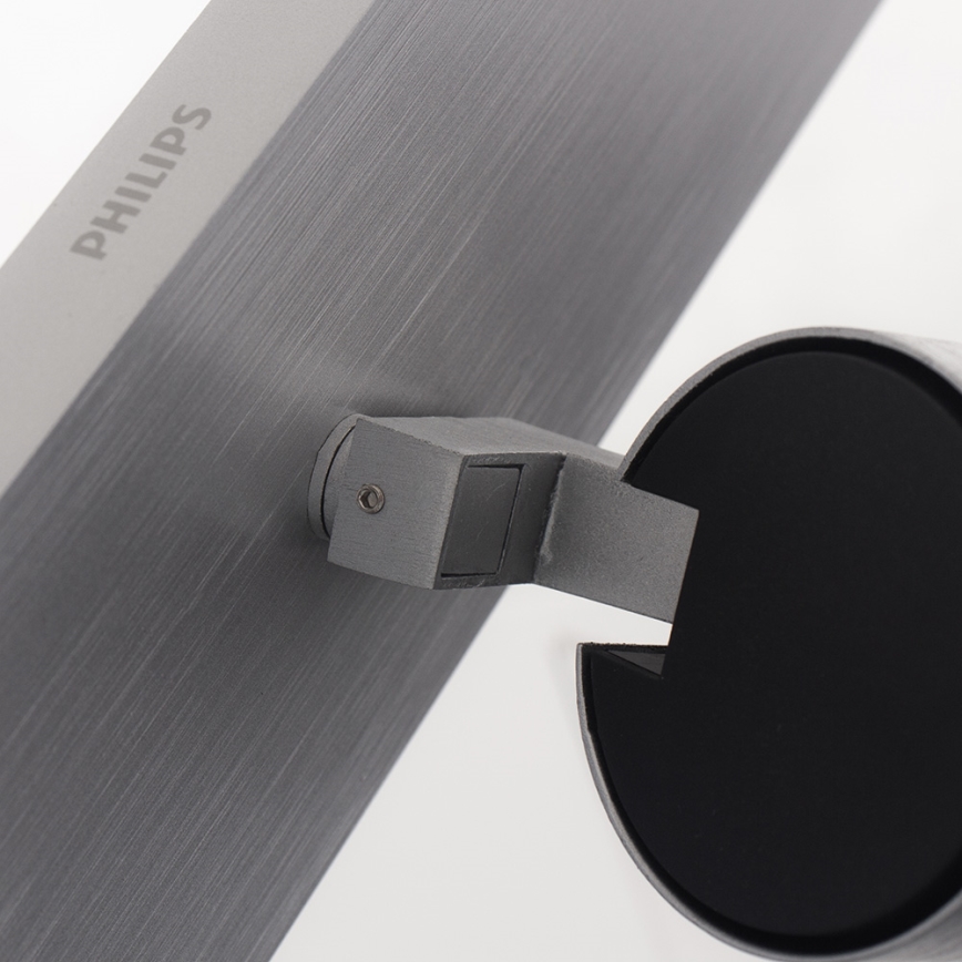 Kovová doska s nápisom „PHILIPS“ je pripevnená k okrúhlej kovovej základni. Spojenie zabezpečuje kovový držiak.