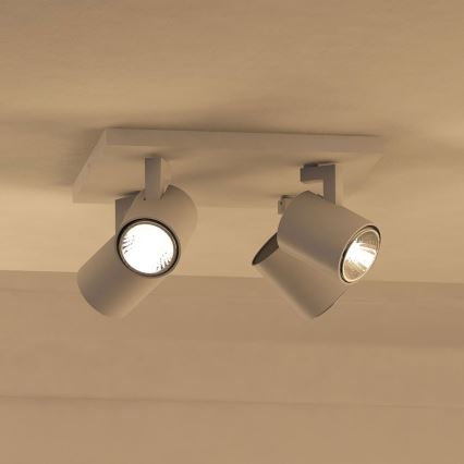 Dvojité stropné svietidlo s valcovými tienidlami svieti na svetlo. Svietidlá sú pripevnené k obdĺžnikovej základni pripevnenej na strope. Svetlo je teplej farby.