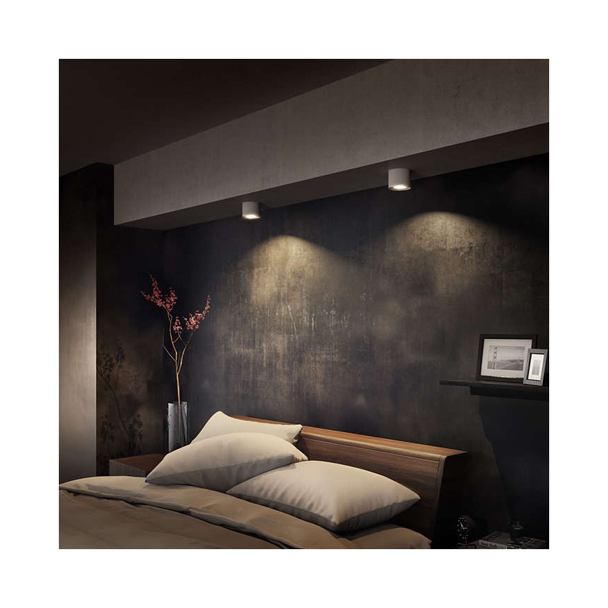 Dve stropné svietidlá osvetľujú spálňu. Svietidlá sú umiestnené na strope nad posteľou s posteľnou bielizňou. Stena za posteľou je tmavo sivá, zdobená.