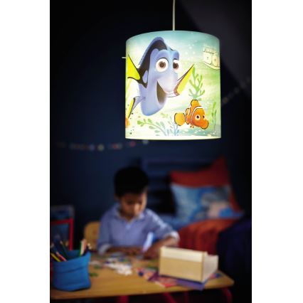 Závesná lampa s motívom rýb z filmu „Hľadaj Dory“ visí v detskej izbe. Dieťa kreslí pri stole pod lampou.