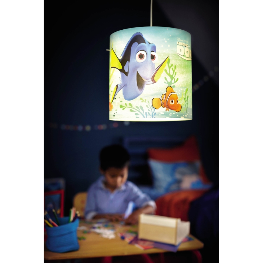 Závesná lampa s motívom rýb z filmu „Hľadaj Dory“ visí v detskej izbe. Dieťa kreslí pri stole pod lampou.