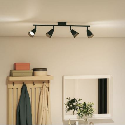 Čtveřice čiernych bodových svietidiel s kužeľovitými tienidlami je pripevnená k stropnej lište. Lišta je namontovaná na strope v miestnosti s dreveným vešiakom na stene a zrkadlom.