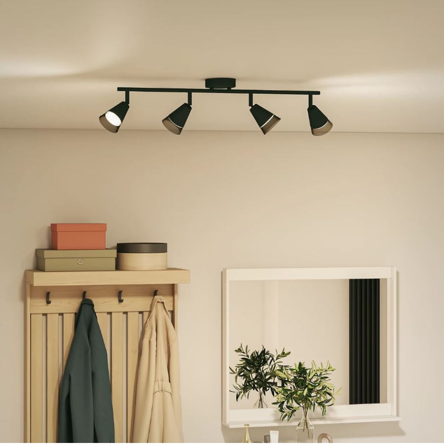 Čtveřice čiernych bodových svietidiel s kužeľovitými tienidlami je pripevnená k stropnej lište. Lišta je namontovaná na strope v miestnosti s dreveným vešiakom na stene a zrkadlom.