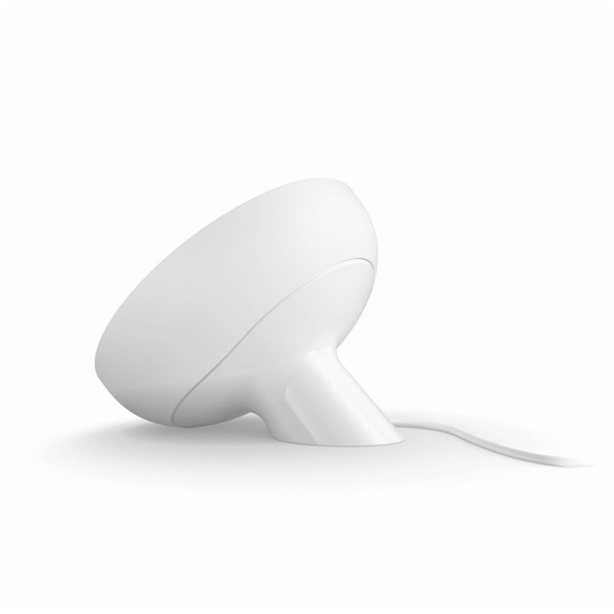 Biela lampa s okrúhlym tienidlom a úzkym podstavcom stojí na bielej ploche. Je pripojená k elektrickej sieti.