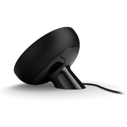 Čierny okrúhly reproduktor s úzkym podstavcom stojí na bielom podklade. K reproduktoru je pripojený kábel.