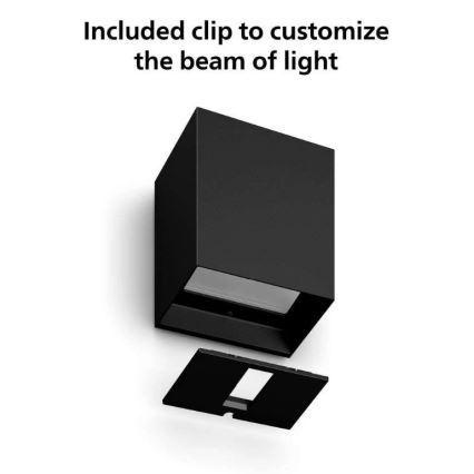 Čierna nástenná lampa s odnímateľným klipom na úpravu svetelného lúča. Klip je umiestnený pod lampou. Text: „Included clip to customize the beam of light“.
