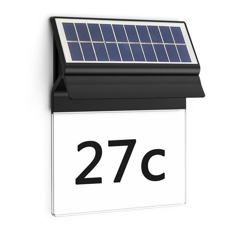 Solárny panel s číslom domu 27c je pripevnený na stenu. Panel nabíja podsvietenie čísla. Je to vonkajšia inštalácia na bielom pozadí.
