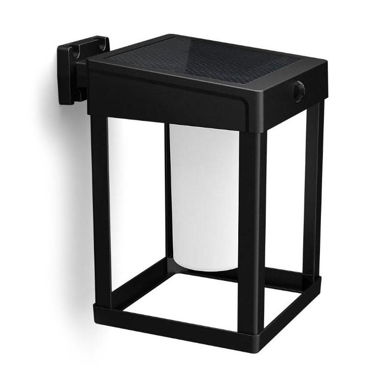 Solárna lampa je pripevnená na stenu. Má štvorcový čierny rám, vnútri valcový biely svetelný zdroj a na vrchu solárny panel.