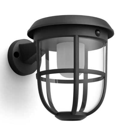 Solárna nástenná lampa s čírym skleneným tienidlom a čiernym kovovým rámom je pripevnená na stenu. Lampa má zabudovaný pohybový senzor.