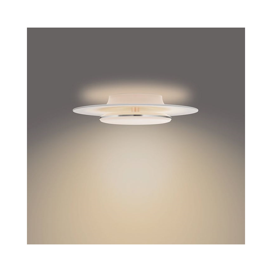 Svietidlo svieti na strop. Má dva kruhové difúzory, horný väčší a spodný menší, s kovovým lemom medzi nimi. Svetlo je teplé, rozptýlené po stene.