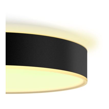 Okrúhle stropné svietidlo s čiernym stredom a svetlozeleným okrajom svieti. Je pripevnené k stropu.