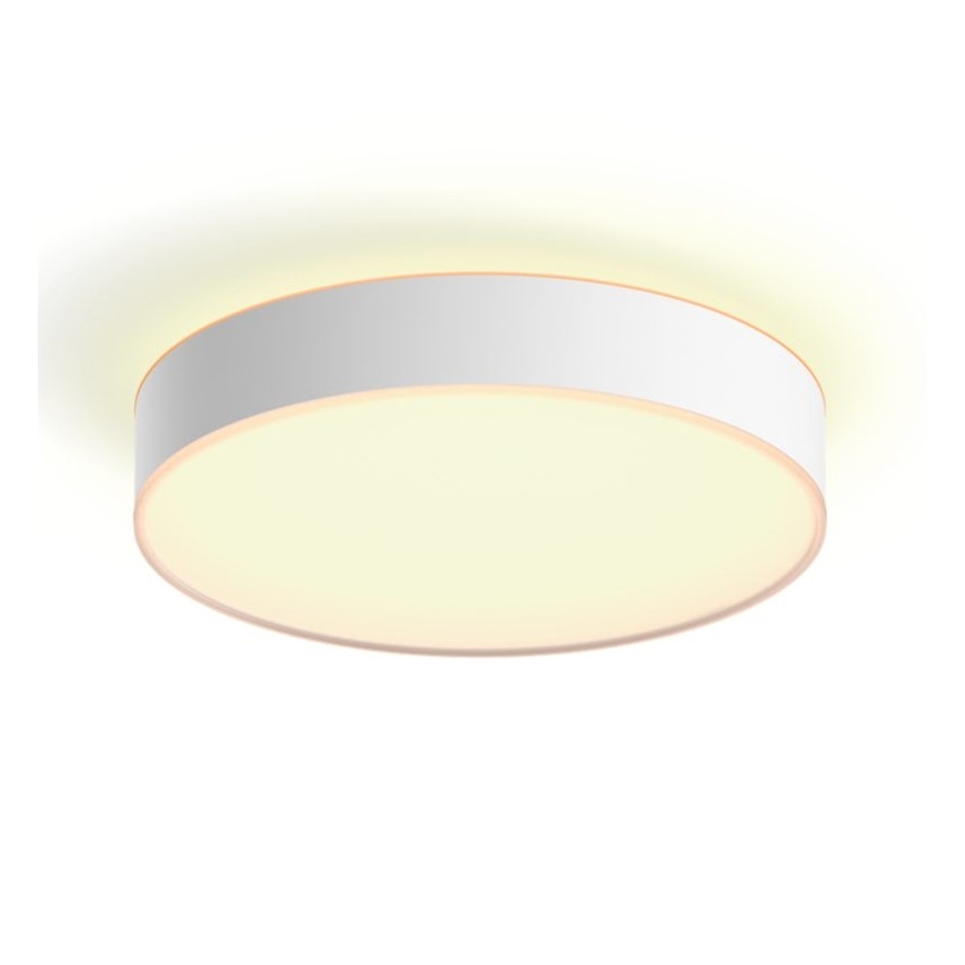 Okrúhle stropné svietidlo s bielym rámom a svetložltým difúznym svetlom je pripevnené k stropu. Svietidlo svieti. Prostredie je svetlé a jednoduché.