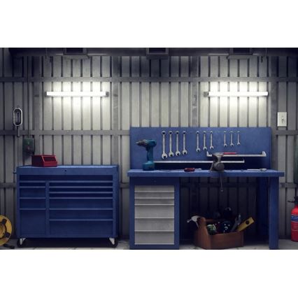 Pracovný stôl s náradím a náradníkový vozík stoja v dielni. Na stole sú umiestnené skrutkovač, kľúče a iné náradie. Steny sú z kovového plechu, osvetlené fluorescenčnými svietidlami.