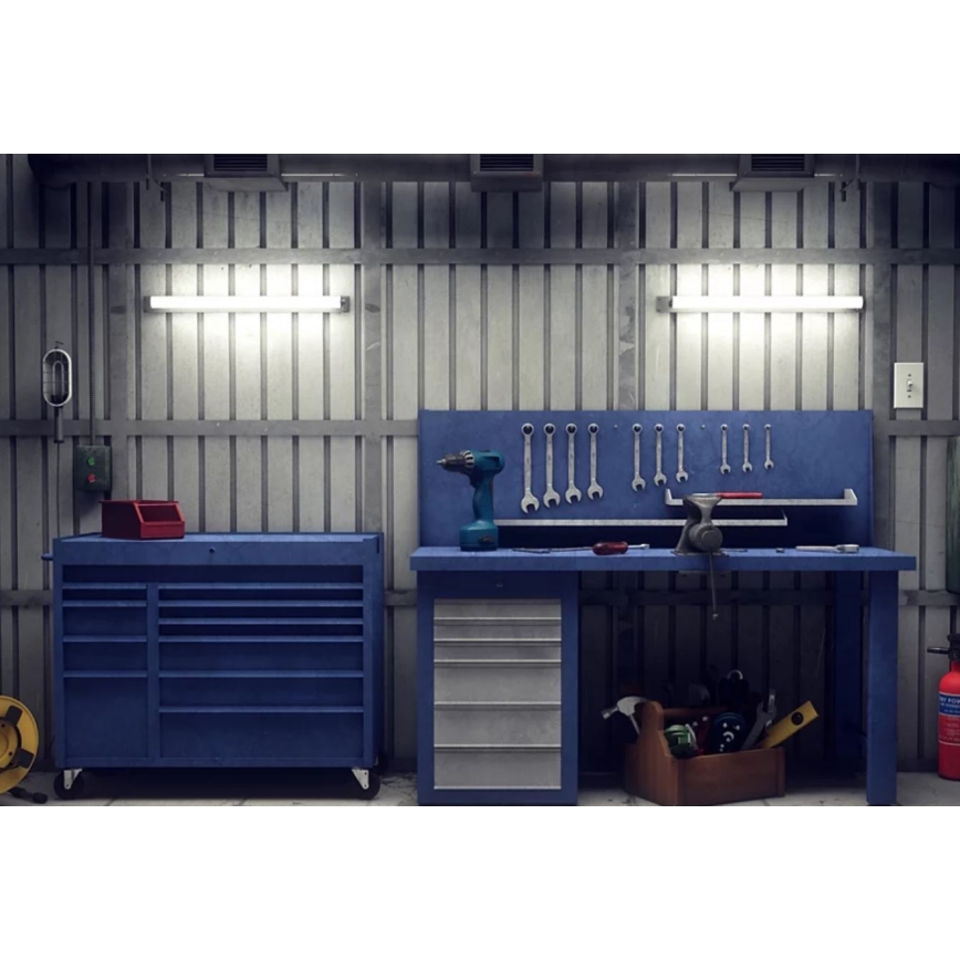 Pracovný stôl s náradím a náradníkový vozík stoja v dielni. Na stole sú umiestnené skrutkovač, kľúče a iné náradie. Steny sú z kovového plechu, osvetlené fluorescenčnými svietidlami.