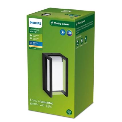 Balenie vonkajšieho LED nástenného svietidla Philips. Svietidlo je čierne, obdĺžnikové s bielym difúzorom. Balenie je zelené s popisom: LED Outdoor Wall Light, Mains power, All weather proof, High quality, Powerful light, Durable design. Nápis na spodku: Enjoy a beautiful garden with light.