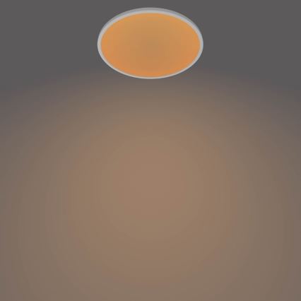 Okrúhle stropné svetlo svieti v tmavohnedej miestnosti. Svetlo má oranžovú plochu a biely rám.