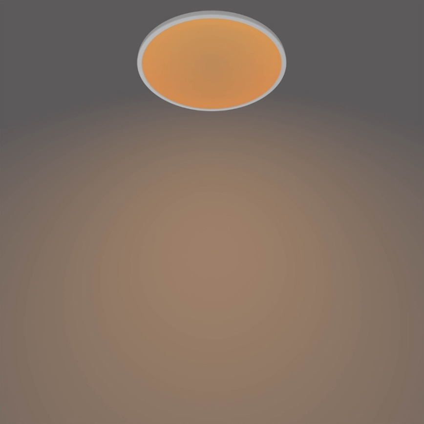 Okrúhle stropné svetlo svieti v tmavohnedej miestnosti. Svetlo má oranžovú plochu a biely rám.