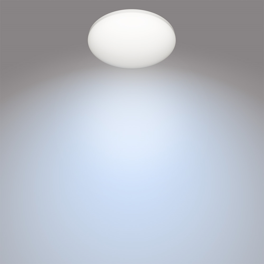 Okrúhle stropné svietidlo svieti na svetlomodrú stenu. Svietidlo je pripevnené k stropu šedej farby.