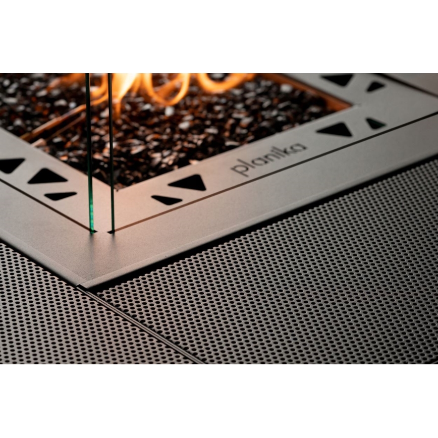 Plynový krb Planika horí, je vsadený do kovového rámu s perforovaným dnom a sklenenými štítkami.